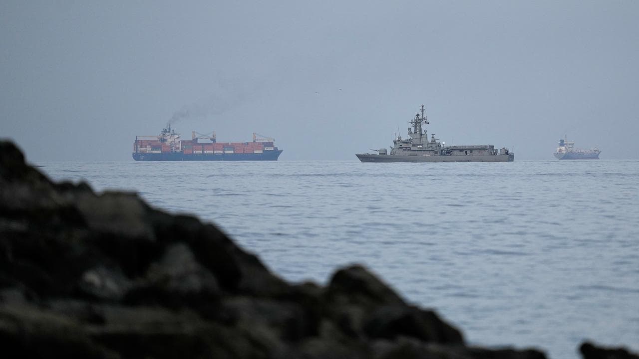 A UAE navy ship sails next to a cargo ship in the Strait of Hormuz