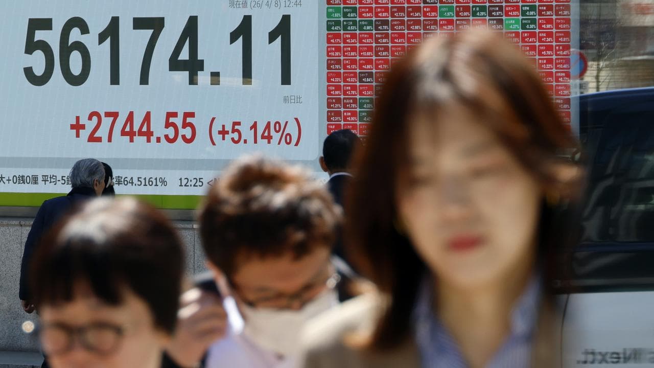 Passers-by walk past a stock market indicator board in Tokyo, Japan
