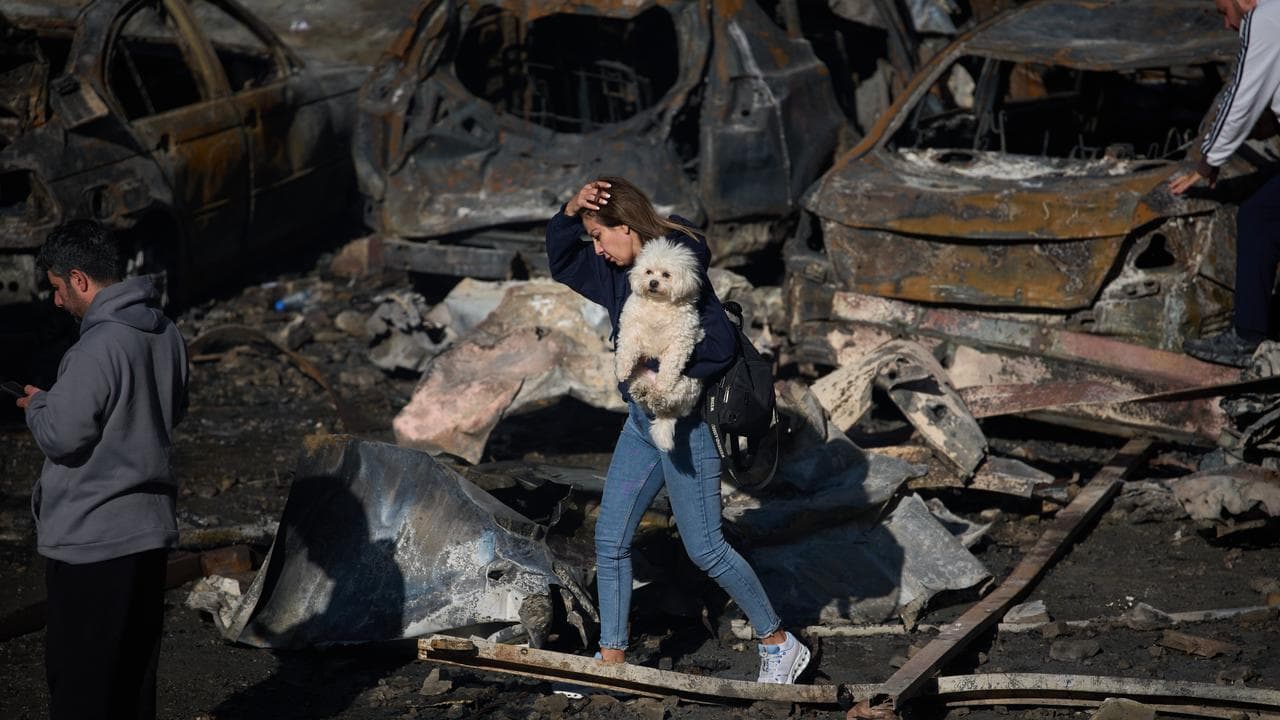 A woman walks past burned cars after and Israeli airstrike in Beirut