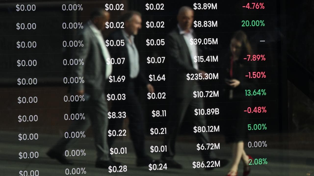 Pedestrians are seen reflected in a screen showing stock information