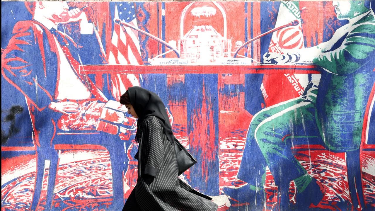 An Iranian woman walks past an anti-US mural in Tehran, Iran