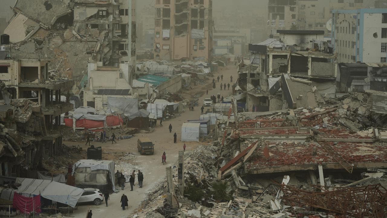 Palestinians walk on a Gaza street surrounded by buildings destroyed