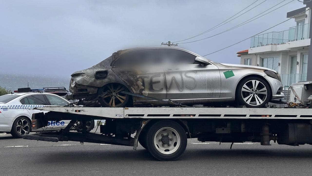 A burnt out car with blurred anti-Semitic graffiti