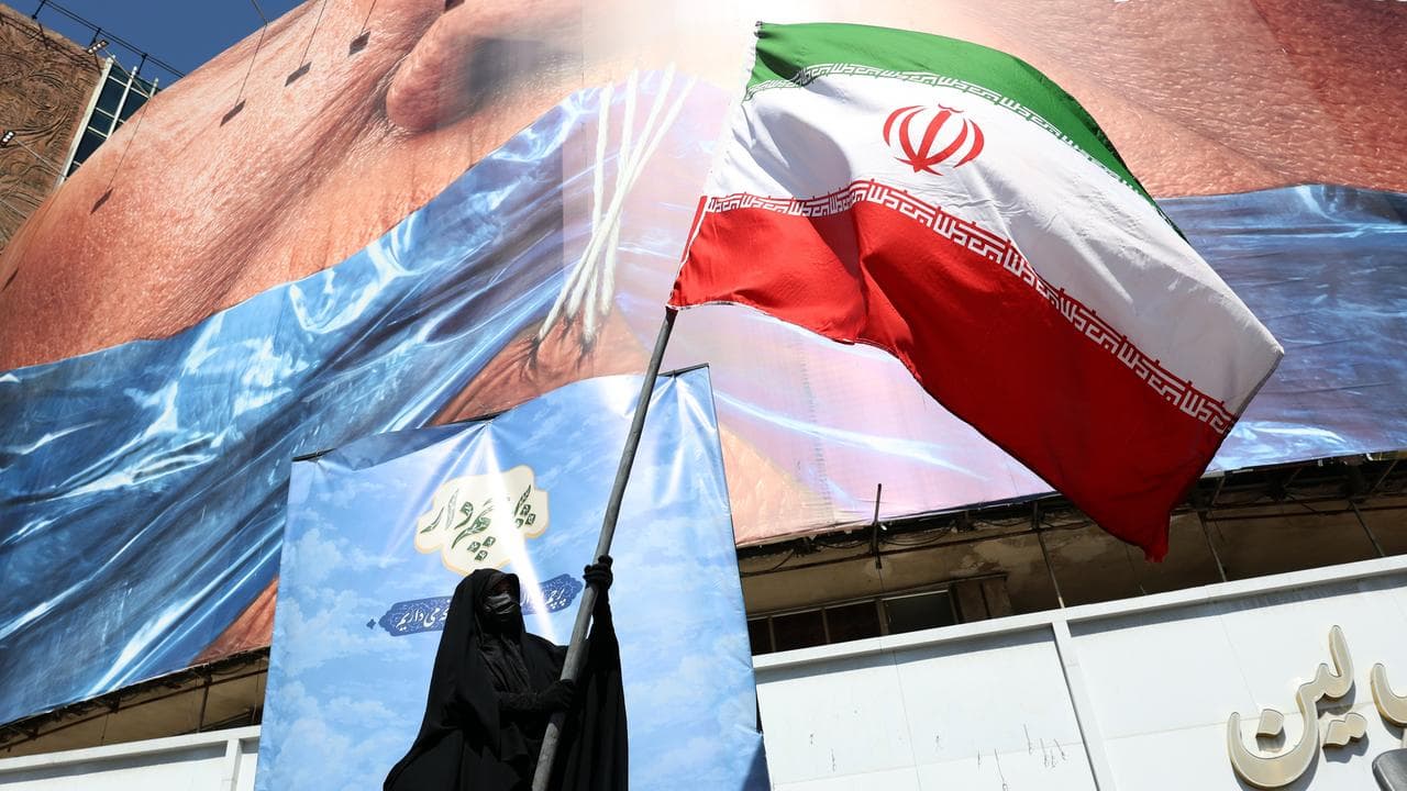 A woman holds Iran’s national flag in front of an anti-US billboard