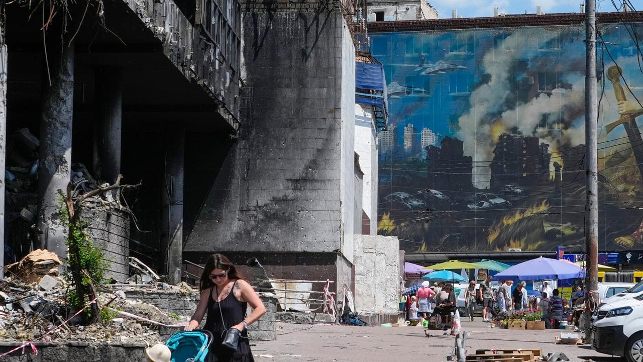 A mother pushes a stroller past a damaged building in Kyiv