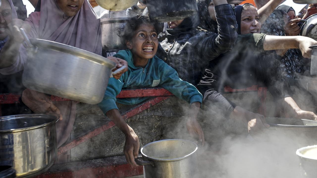 Displaced Palestinian children hold pots as they receive food