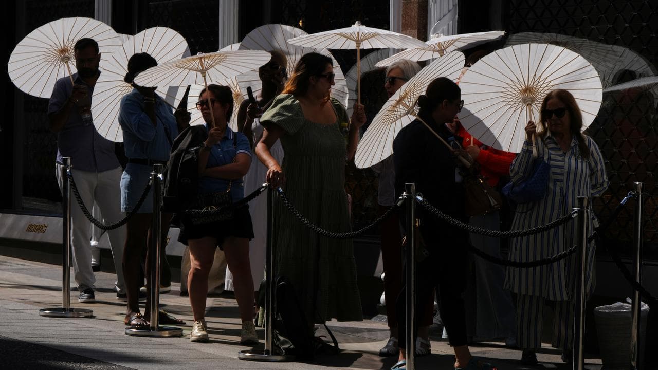People use parasols as they queue outside a shop in London