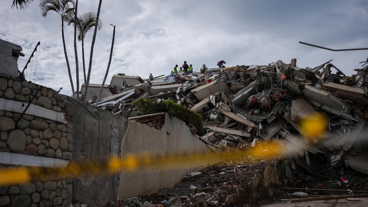 Rescue workers stand on the rubble of a building that collapsed