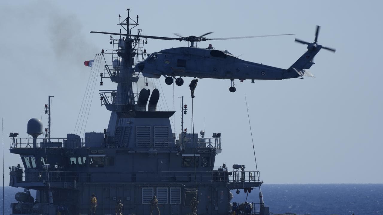 A helicopter loads marines over a naval ship during a NATO exercise