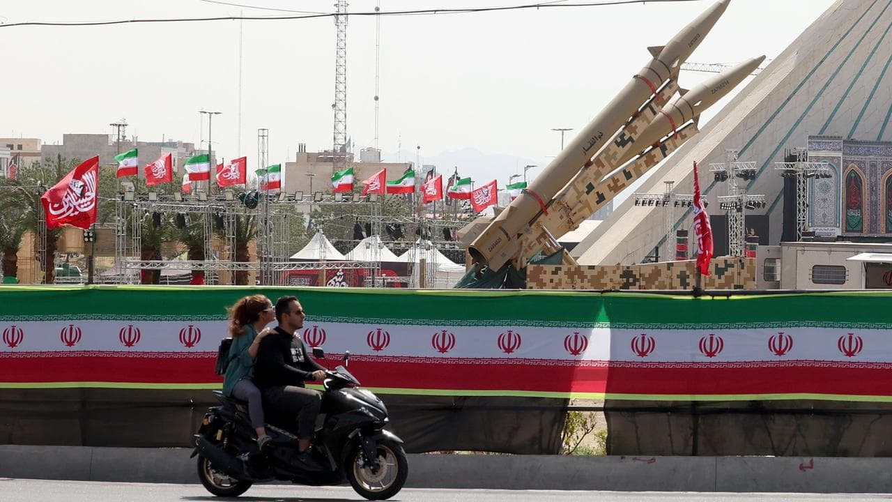 A couple rides a motorbike next to Iranian missiles