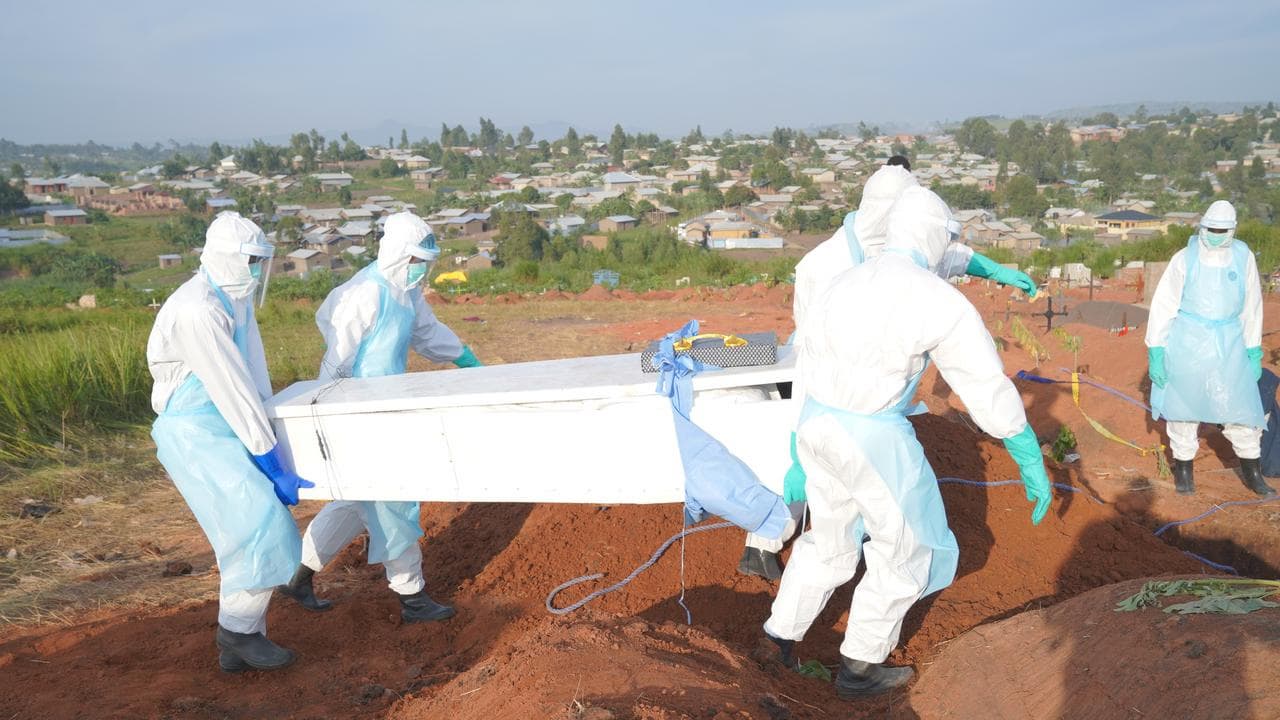 People dressed in protective gear carry a coffin
