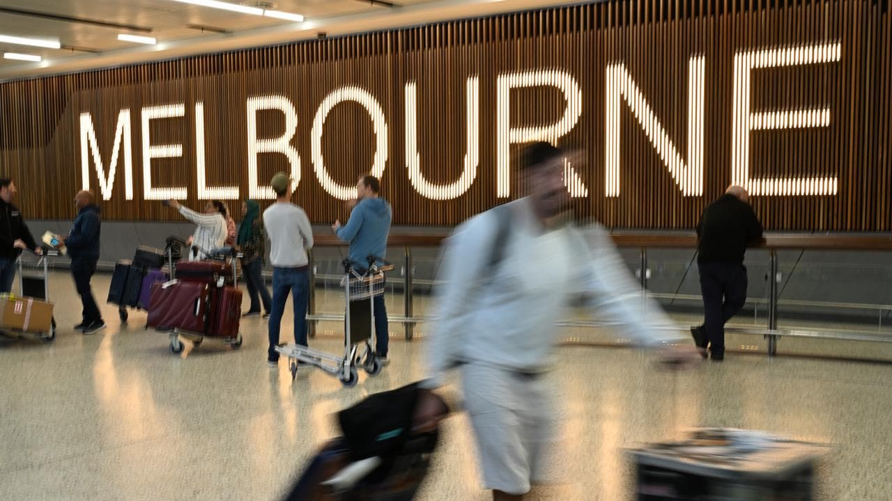 Travellers pass by the Melbourne sign at the airport