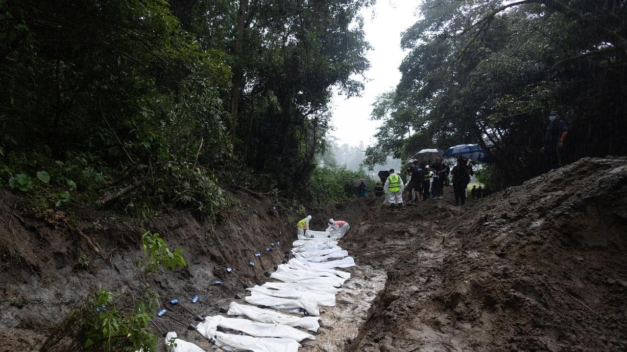 Officers place the bodies of unidentified victims into a mass grave