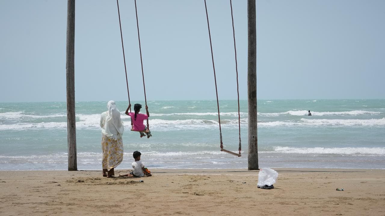 A woman pushes a girl on a swing on a beach
