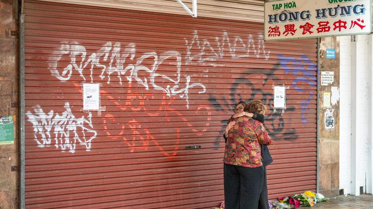 Two women comfort each other outside the Hong Hung Asian Grocer