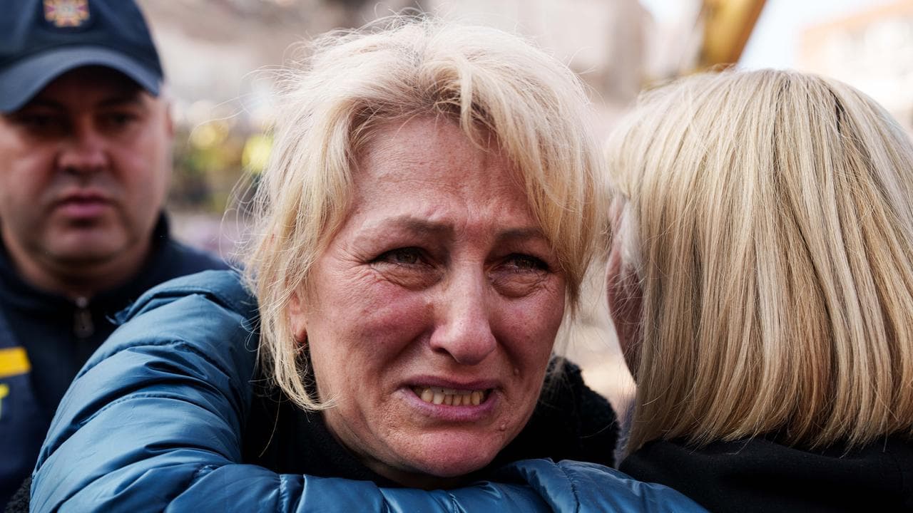A woman standing next to the destroyed building tearfully reacts.