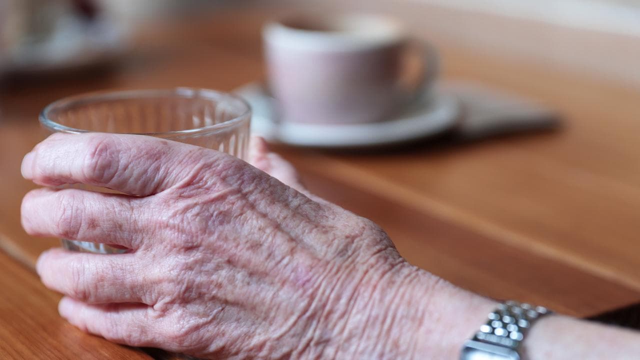 An elderly person holds a cup